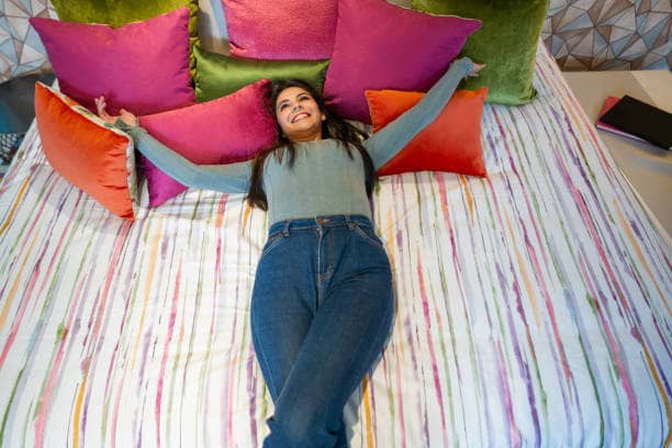 Heureuse femme latino-américaine achetant un lit dans un magasin de meubles et s'allongeant pour essayer le confort du matelas tout en souriant.